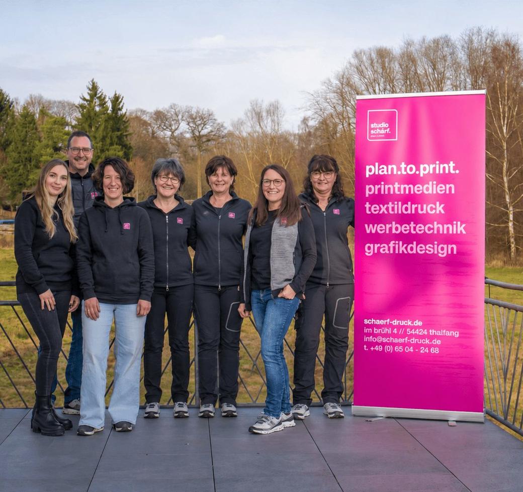 Das Team von studio schärf. neben einem Roll-Up mit der Aufschrift plan.to.print